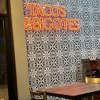 Red Tacos El Bigotes neon sign on a black and white tile wall in the dining room