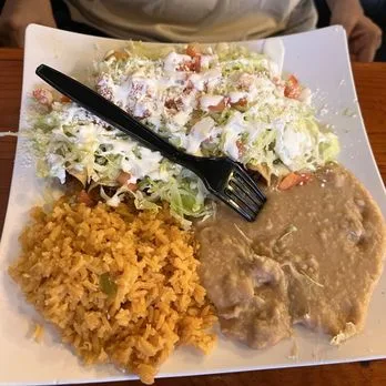 Antojito plate topped with lettuce, crema, cotija and pico de gallo, with Mexican rice and refried beans
